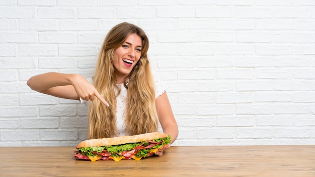 Giovane donna bionda felice che tiene un grande panino