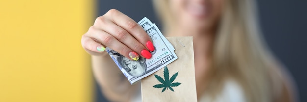 Giovane donna bionda felice che tiene un pacco con marijuana e consegna di denaro di cannabis legale