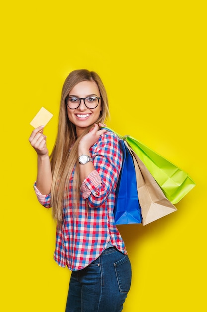 Giovane donna bionda felice in vetri che tengono la carta di credito e sacchetti della spesa variopinti