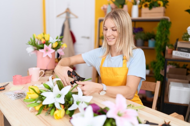 Giovane donna bionda fiorista taglio bouquet di fiori al negozio di fiori