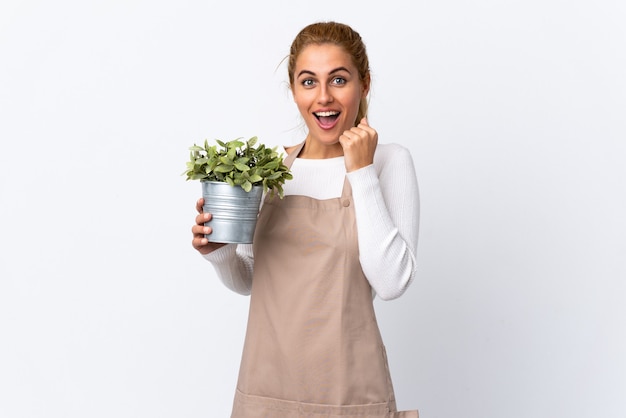 Giovane donna bionda giardiniere donna che tiene una pianta isolata che celebra una vittoria