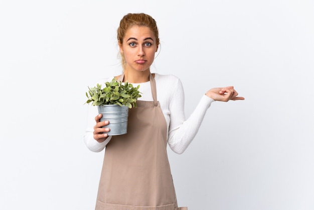 Giovane donna bionda giardiniere donna che tiene una pianta isolata