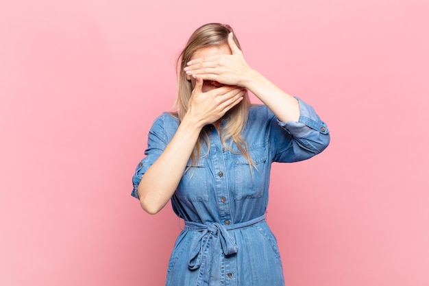 giovane donna bionda graziosa che copre il viso con entrambe le mani dicendo no alla telecamera! rifiutare le foto o vietare le foto