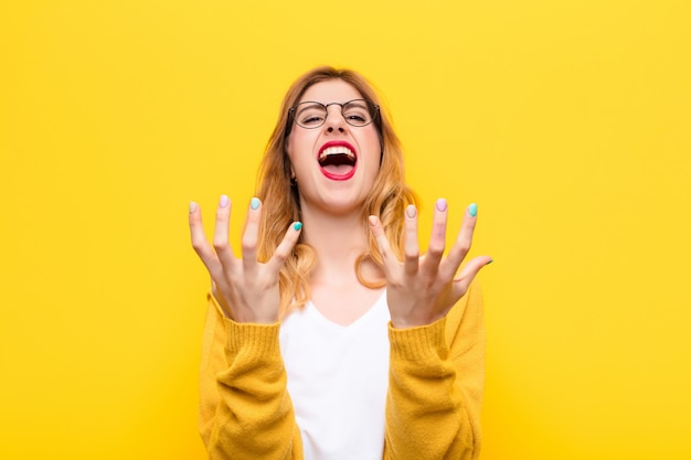 Giovane donna bionda graziosa che sembra disperata e frustrata, stressata, infelice e infastidita, che grida e che grida contro la parete gialla