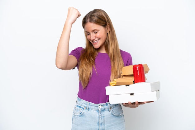 Giovane donna bionda graziosa che tiene un fast food isolato su sfondo bianco che celebra una vittoria