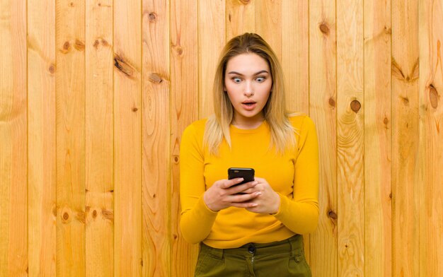 Giovane donna bionda graziosa con un telefono cellulare contro la parete di legno