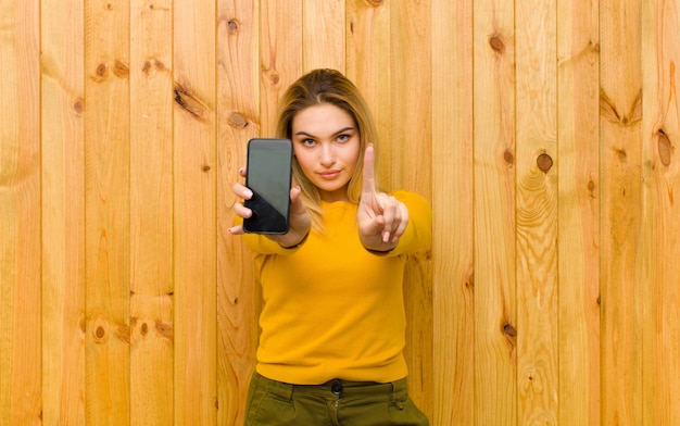 Giovane donna bionda graziosa con un telefono cellulare contro la parete di legno