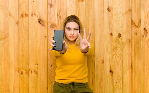 Giovane donna bionda graziosa con un telefono cellulare contro la parete di legno