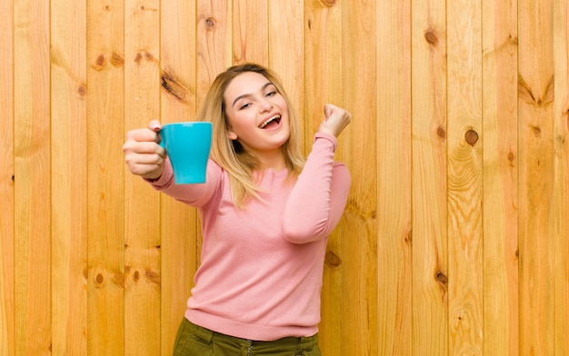 Giovane donna bionda graziosa con una parete di legno della tazza di caffè