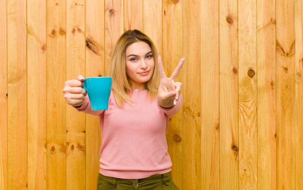 Giovane donna bionda graziosa con una tazza di caffè contro la parete di legno