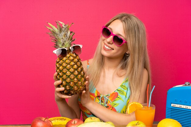 Giovane donna bionda in costume da bagno in possesso di un ananas con occhiali da sole