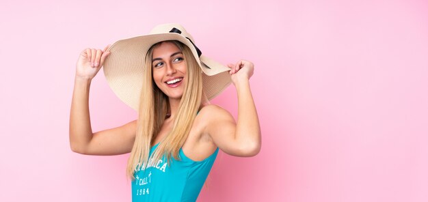 Giovane donna bionda in costume da bagno nelle vacanze estive sopra la parete rosa isolata