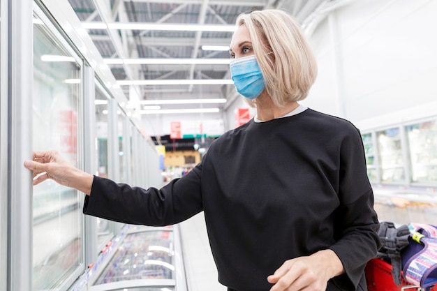 Giovane donna bionda in maschera in un supermercato. Pandemia di coronavirus.
