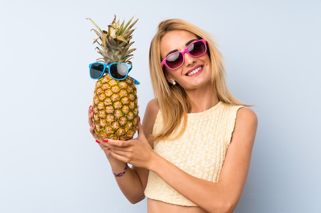 Giovane donna bionda in possesso di un ananas con occhiali da sole