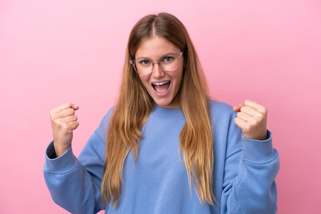 Giovane donna bionda isolata su sfondo rosa Con gli occhiali e celebrando una vittoria