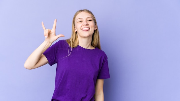 Giovane donna bionda isolata su sfondo viola che mostra un gesto di corna come un concetto di rivoluzione.