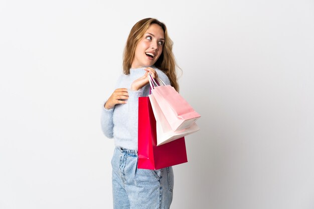 Giovane donna bionda isolata sui sacchetti della spesa bianchi della tenuta e sul sorridere