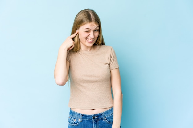 Giovane donna bionda isolata sul muro blu che copre le orecchie con le mani.
