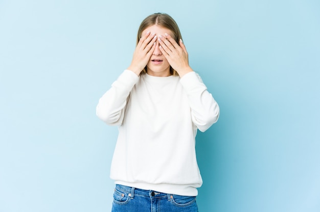 Giovane donna bionda isolata sul muro blu paura che copre gli occhi con le mani.