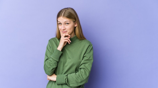 Giovane donna bionda isolata sul muro viola contemplando, pianificando una strategia, pensando al modo di fare impresa.