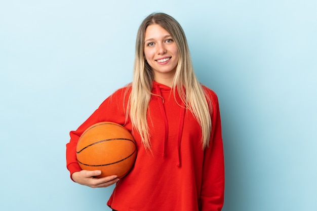 Giovane donna bionda isolata sulla parete blu che gioca a pallacanestro
