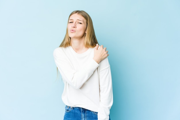 Giovane donna bionda isolata sulla parete blu che ha un dolore alla spalla