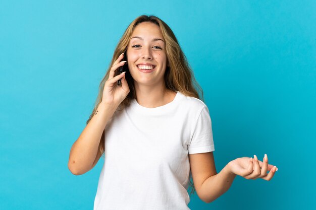 Giovane donna bionda isolata sulla parete blu mantenendo una conversazione con il telefono cellulare con qualcuno