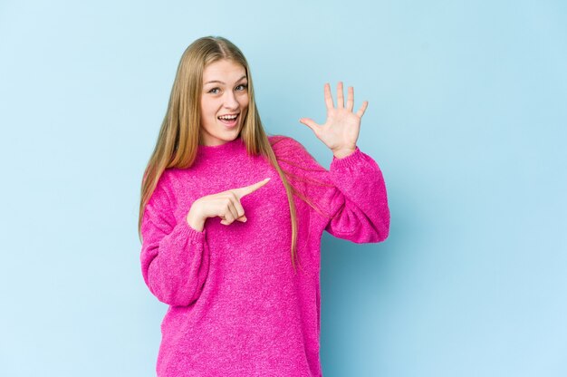 Giovane donna bionda isolata sulla parete blu sorridente allegro che mostra il numero cinque con le dita.