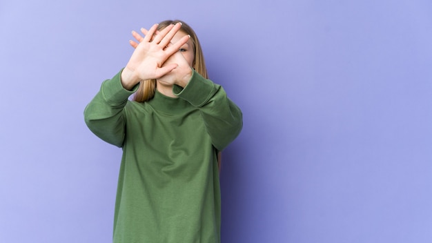 Giovane donna bionda isolata sulla parete viola mantenendo due braccia incrociate, concetto di negazione.