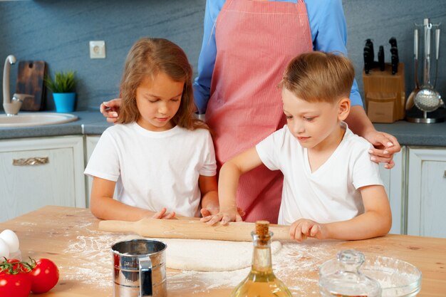 Giovane donna bionda, madre e figli che si divertono durante la cottura della pasta