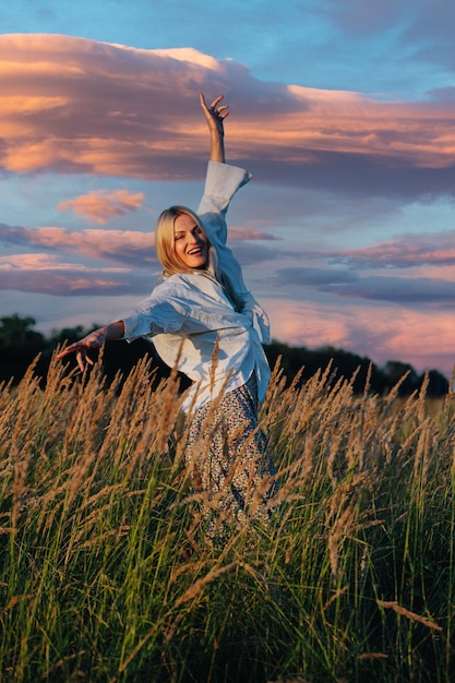 Giovane donna bionda rilassata felice che osserva in mezzo al campo di grano