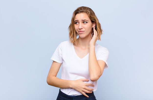 Giovane donna bionda sentirsi stressata, frustrata e stanca, sfregando il collo doloroso, con uno sguardo preoccupato e preoccupato contro la parete di colore piatto