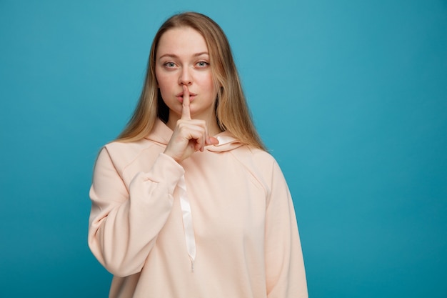 Giovane donna bionda seria che fa gesto di silenzio