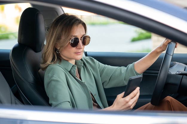 Giovane donna bionda seria che scorre in smartphone