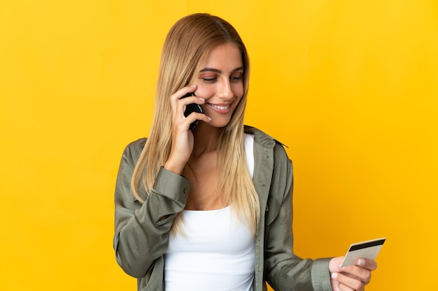 Giovane donna bionda sopra l'acquisto di muro isolato con il cellulare con carta di credito