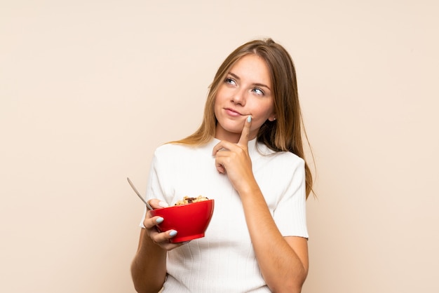 Giovane donna bionda sopra la parete isolata che tiene una ciotola di cereali e di pensiero