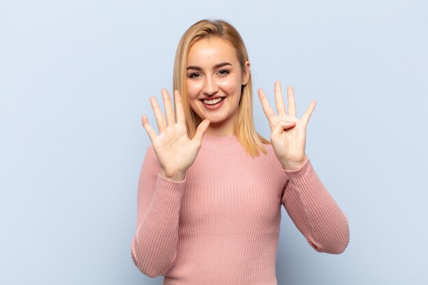 Giovane donna bionda sorridente e guardando amichevole, mostrando il numero nove o nono con la mano in avanti, il conto alla rovescia