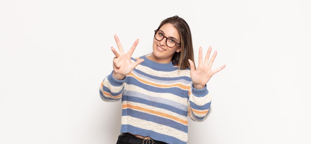 Giovane donna bionda sorridente e guardando amichevole, mostrando il numero nove o nono con la mano in avanti, il conto alla rovescia