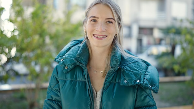 Giovane donna bionda sorridente fiducioso che mostra le parentesi graffe al parco