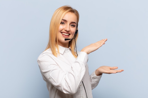 Giovane donna bionda sorridente, sentendosi felice, positiva e soddisfatta, tenendo o mostrando un oggetto o un concetto sullo spazio della copia