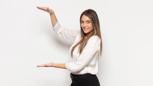 Giovane donna bionda sorridente, sentendosi felice, positiva e soddisfatta, tenendo o mostrando un oggetto o un concetto