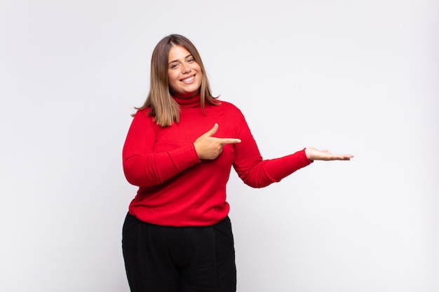 Giovane donna bionda sorridente, sentendosi felice, spensierata e soddisfatta, indicando un concetto o un'idea sullo spazio della copia sul lato