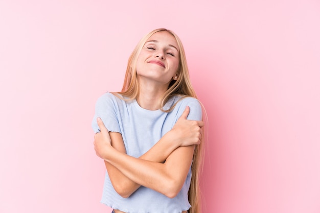 Giovane donna bionda su sfondo rosa abbracci, sorridente spensierato e felice.