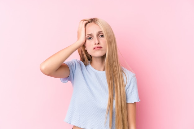 Giovane donna bionda su sfondo rosa stanco e molto assonnato tenendo la mano sulla testa.