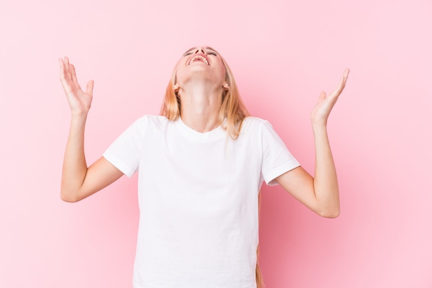 Giovane donna bionda sulla parete rosa che grida al cielo, alzando lo sguardo, frustrata.