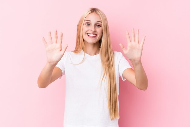 Giovane donna bionda sulla parete rosa che mostra numero dieci con le mani.