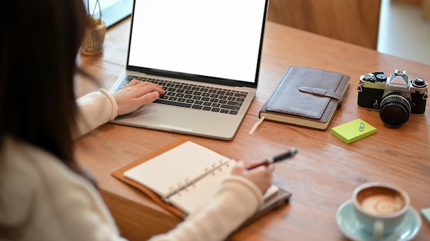 Giovane donna blogger fotografo freelance che lavora al computer portatile mentre prende alcune note sul diario