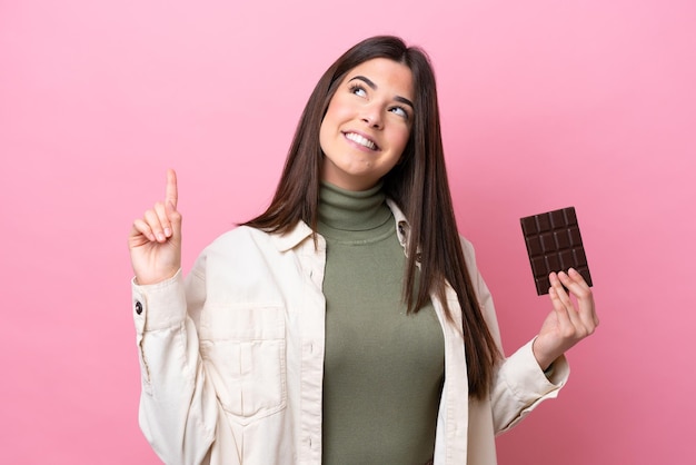 Giovane donna brasiliana con cioccolato isolato su sfondo rosa che indica una grande idea