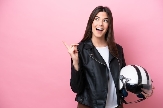 Giovane donna brasiliana con un casco da motociclista isolato su sfondo rosa che intende realizzare la soluzione sollevando un dito