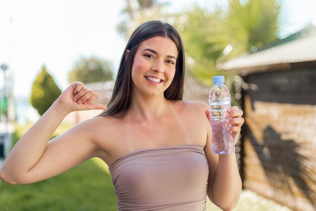 Giovane donna brasiliana con una bottiglia d'acqua all'aperto orgogliosa e soddisfatta di se stessa